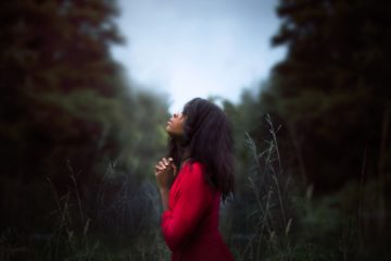 woman wearing red sweatshirt looking at top between trees near grass during daytime